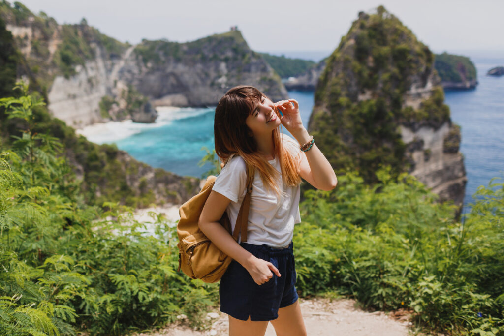 Traveling and adventure concept. Happy pretty woman with back pack  traveling in Indonesia on Nusa Penida island. Amazing cliffs and tropical beach view on background.